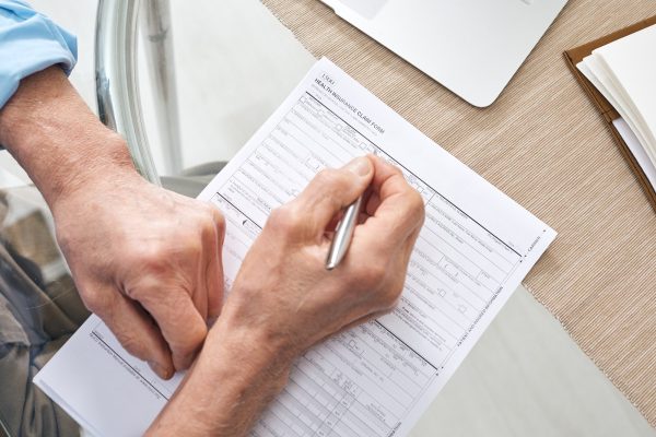 Hands of contemporary senior retired man filling in health insurance form