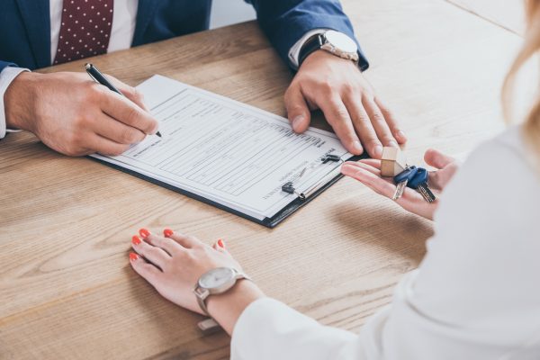 partial view of businesswoman holding house keys near man signing agreement
