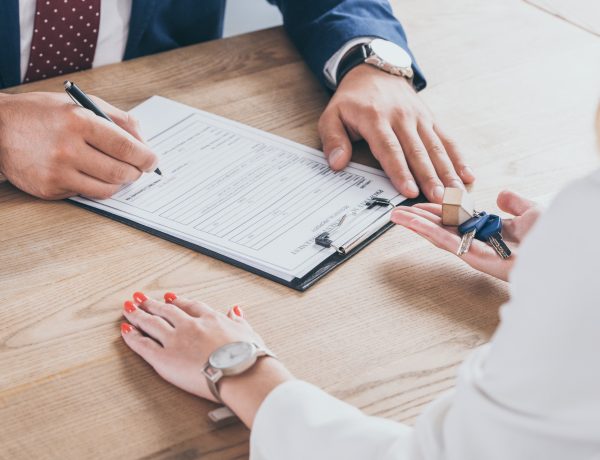partial view of businesswoman holding house keys near man signing agreement
