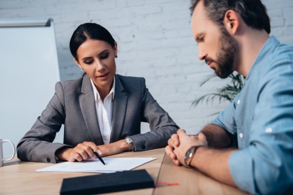 selective focus of brunette lawyer holding pen near insurance documents and bearded client